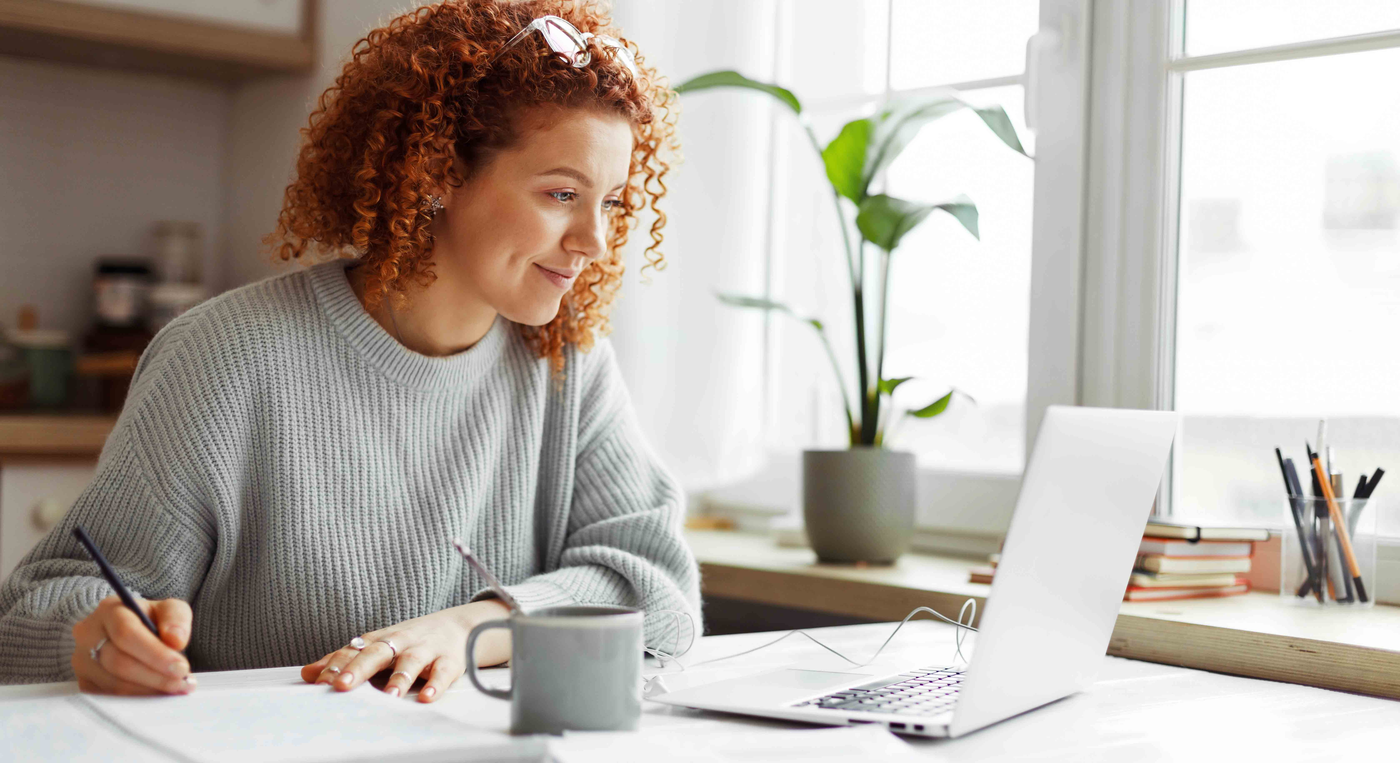 Frau sitzt am Laptop und macht sich Notizen
