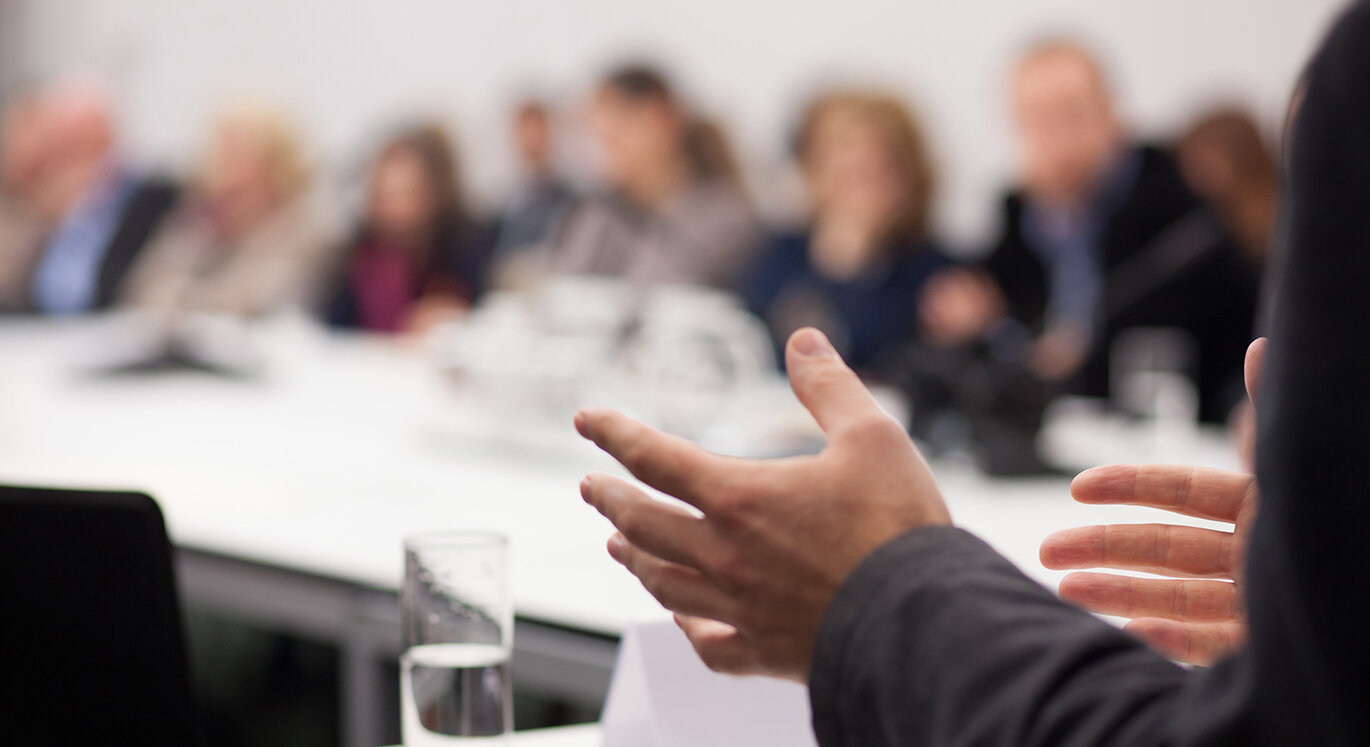 Gruppe von Personen sitzt in einer Besprechung und diskutiert. | © iStock/aerogondo