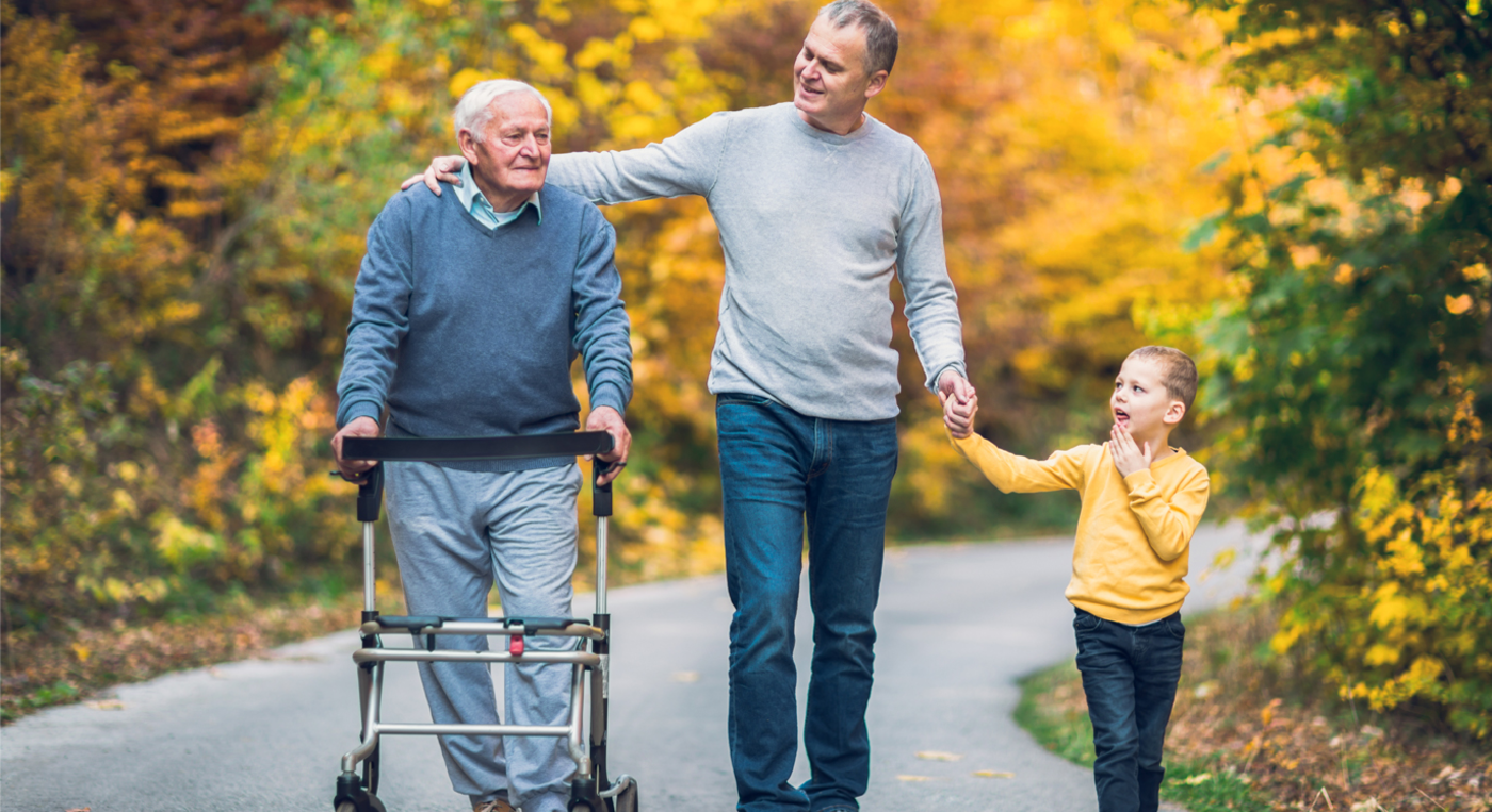 Senior geht mit Rolator und seiner Familie in der Natur spazieren.