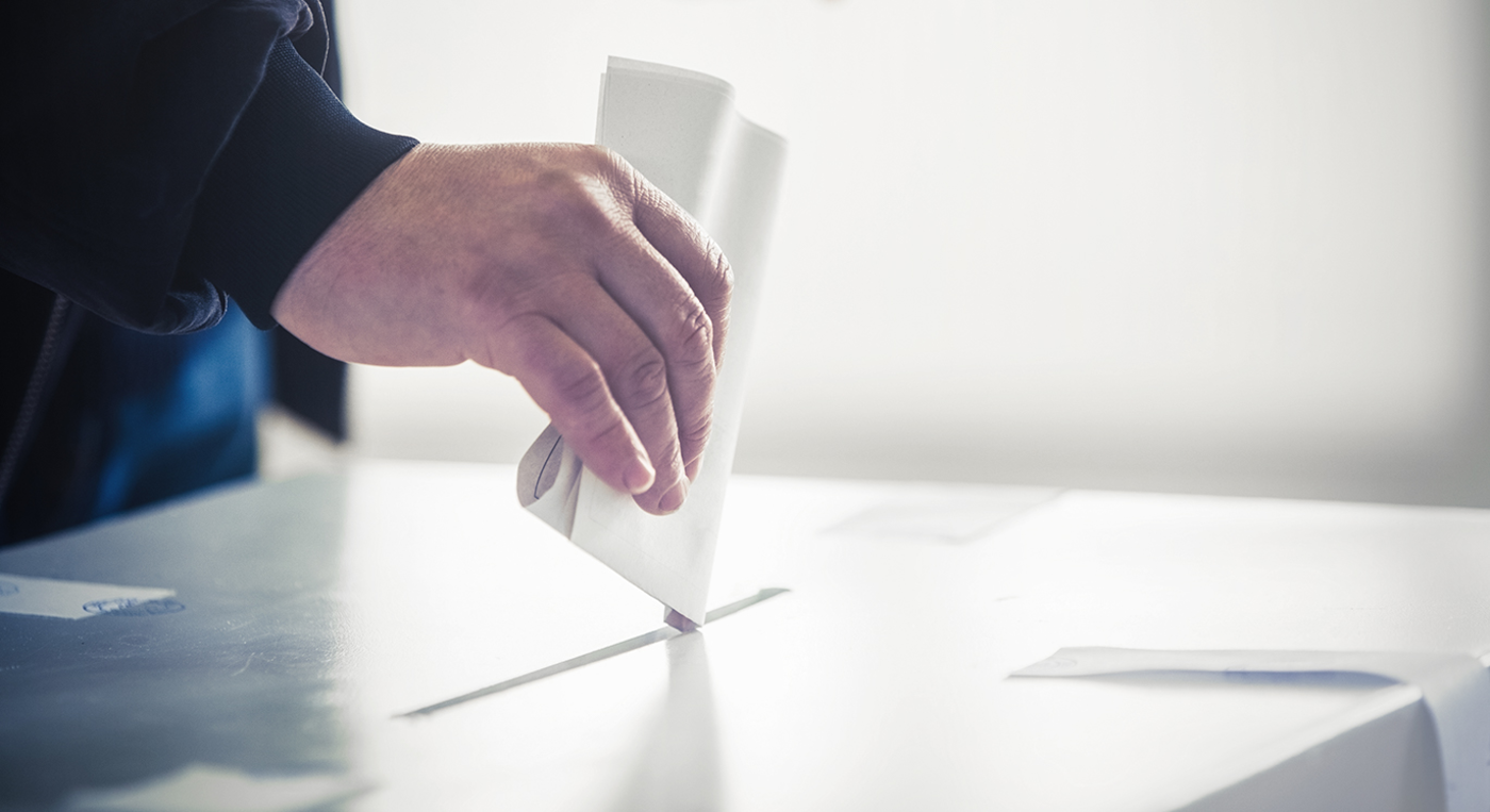 Mann wirft seinen Wahlbrief in eine silberne Wahlurne.