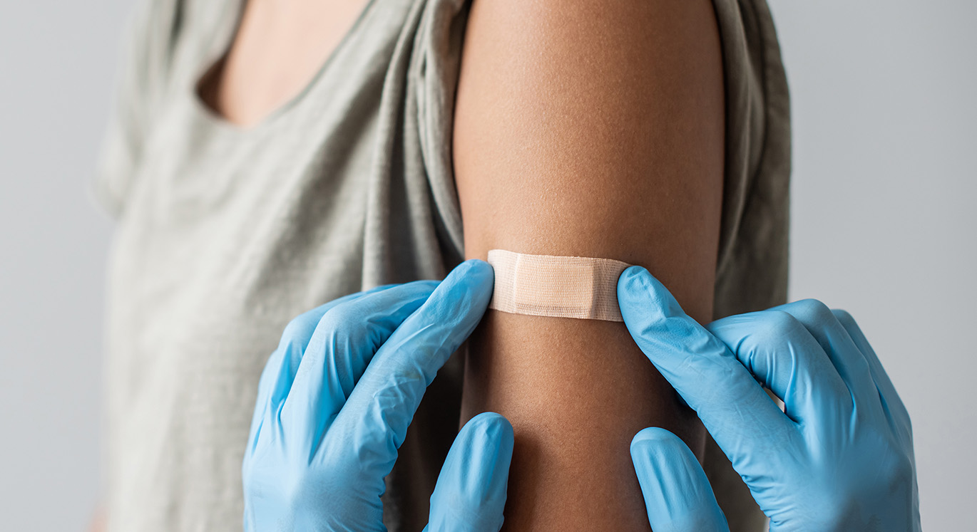 Patientin bekommt nach einer Impfung ein Pflaster auf den Arm geklebt.