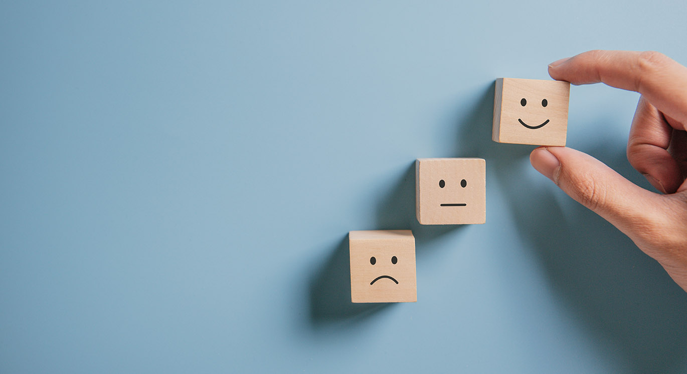 Drei Holzwürfel mit Smileys werden auf einem blauen Hintergrund gelegt.