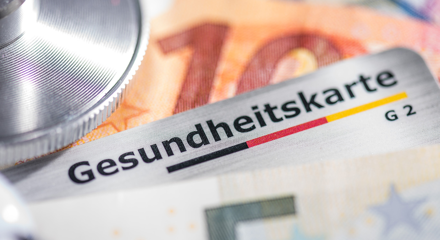 Gesundheitskarte liegt über Geldscheinen auf einem Tisch.