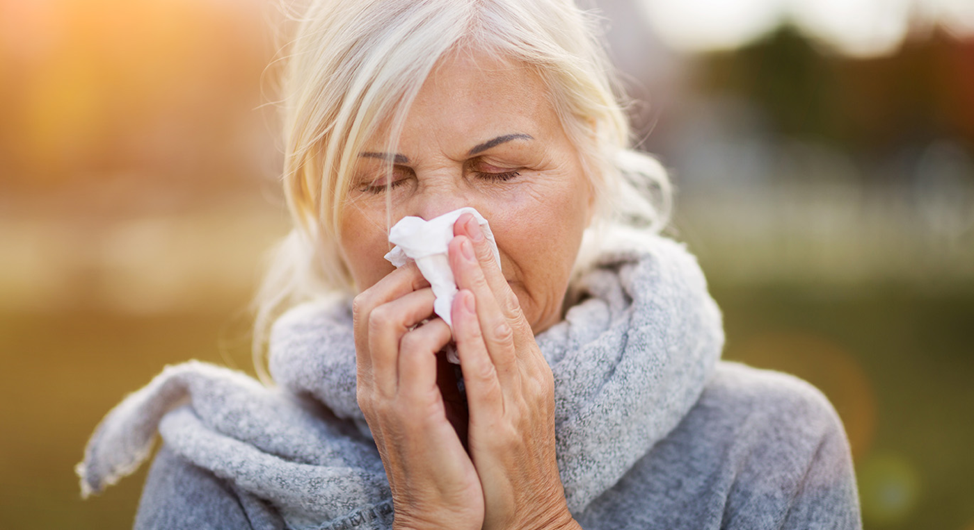 Ältere Patientin trägt einen Schal und putzt beim Spazierengehen im Herbst ihre Nase.