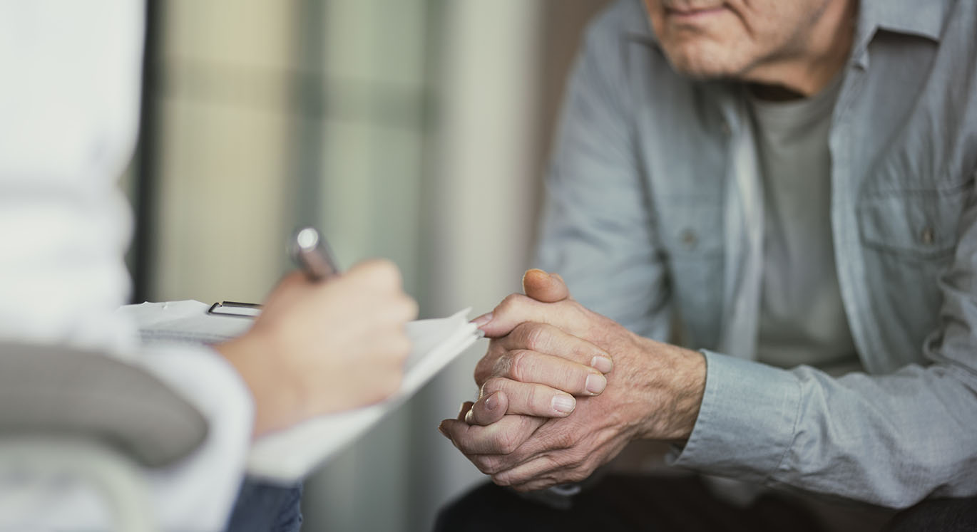 Hausärztin macht sich im Gespräch mit älterem Patient Notizen.