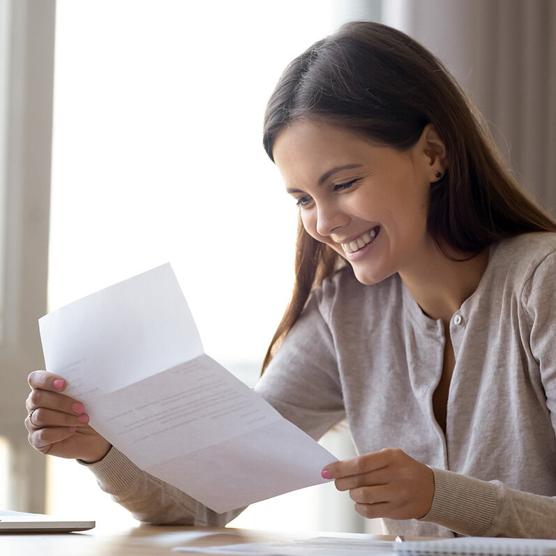 Junge Frau sitzt an einem Schreibtisch und freut sich über einen Brief. | © iStock/fizkes