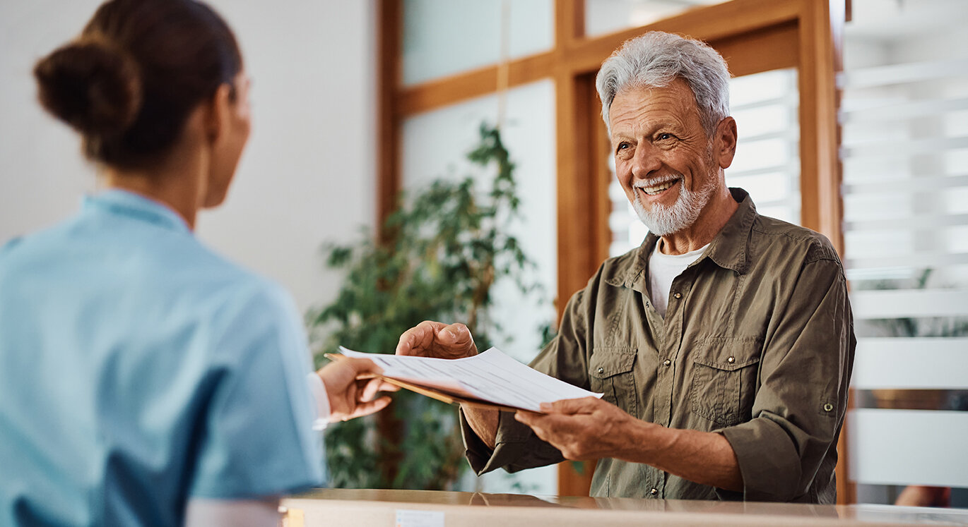 MFA gibt Patient seine Unterlagen für die Einschreibung in die HZV. | © iStock/Drazen Zigic