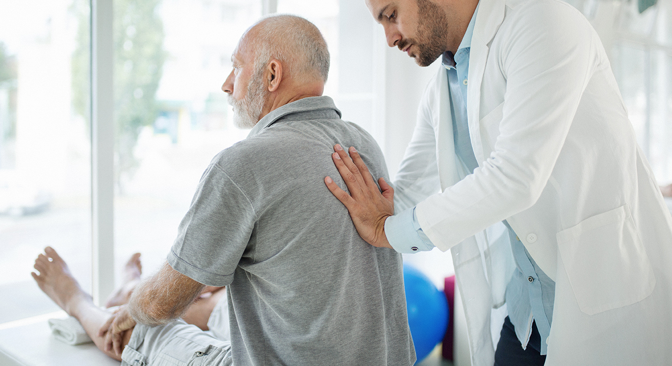 Hausarzt untersucht Patienten am Rücken.