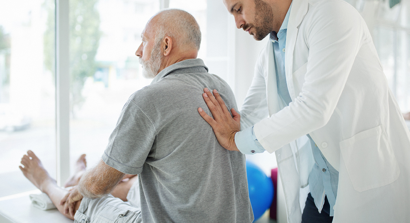 Hausarzt untersucht Patienten am Rücken.